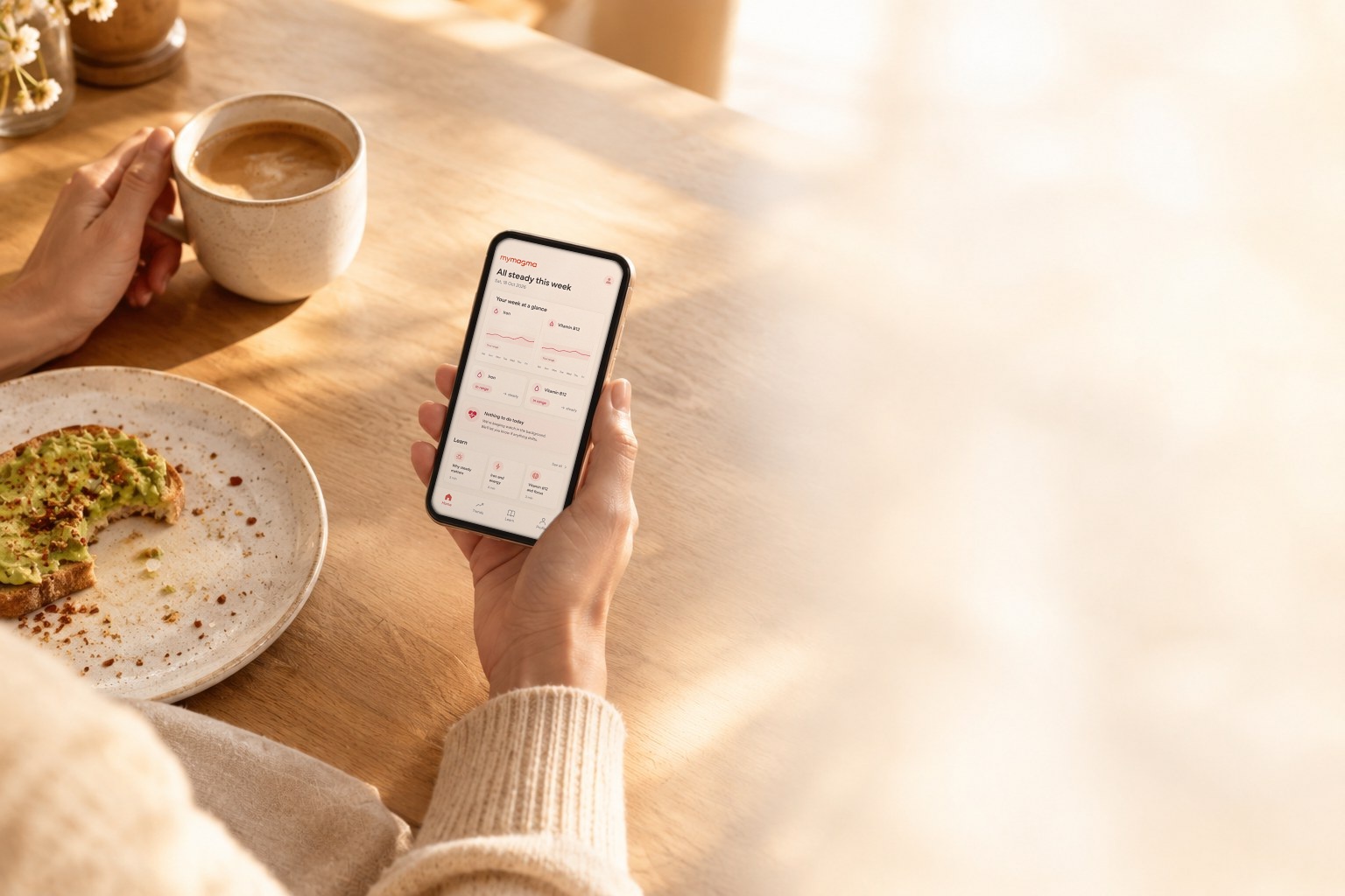 A hand holding a phone with the my magma app's weekly summary, at a sunny breakfast table